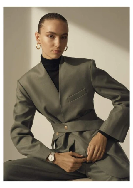 Elegant young woman in stylish green pantsuit with jewelry and wristwatch posing in a studio with minimalist lighting for a fashion editorial.