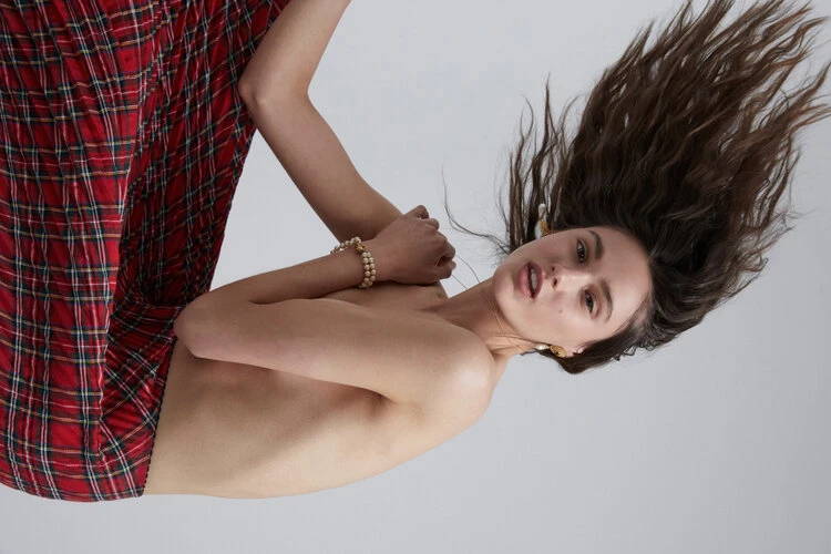 Woman with brown hair and plaid skirt posing in photo studio with white background.
