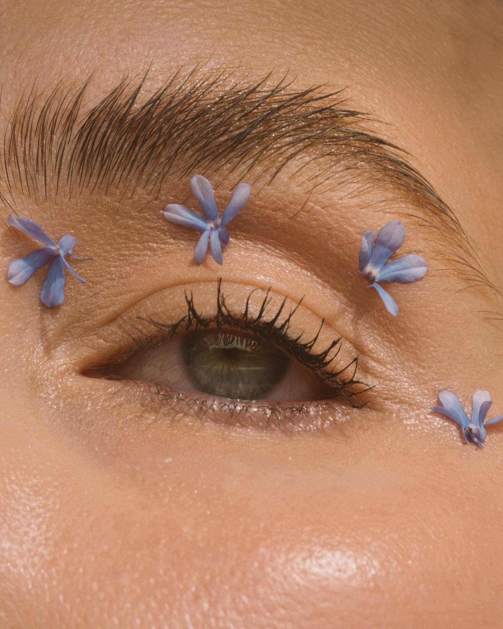 Close-up of a woman's eye with blue flowers, soft lighting, and focus on beauty, skin texture, and delicate floral details.