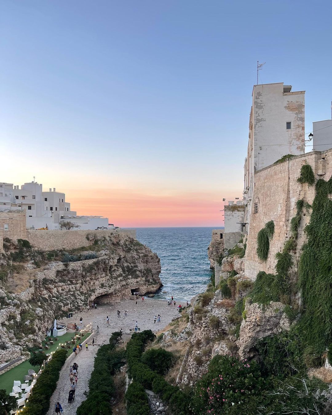 Coastal scene features buildings on cliffs overlooking a beach with people, set against a serene sky during twilight.