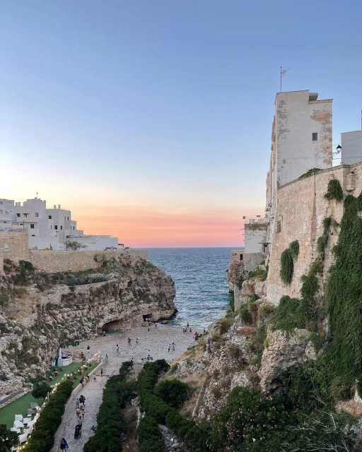 Coastal scene features buildings on cliffs overlooking a beach with people, set against a serene sky during twilight.