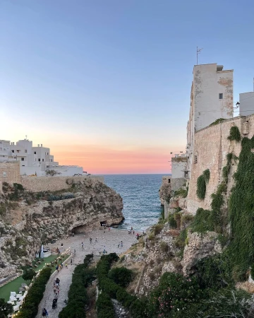 Coastal scene features buildings on cliffs overlooking a beach with people, set against a serene sky during twilight.