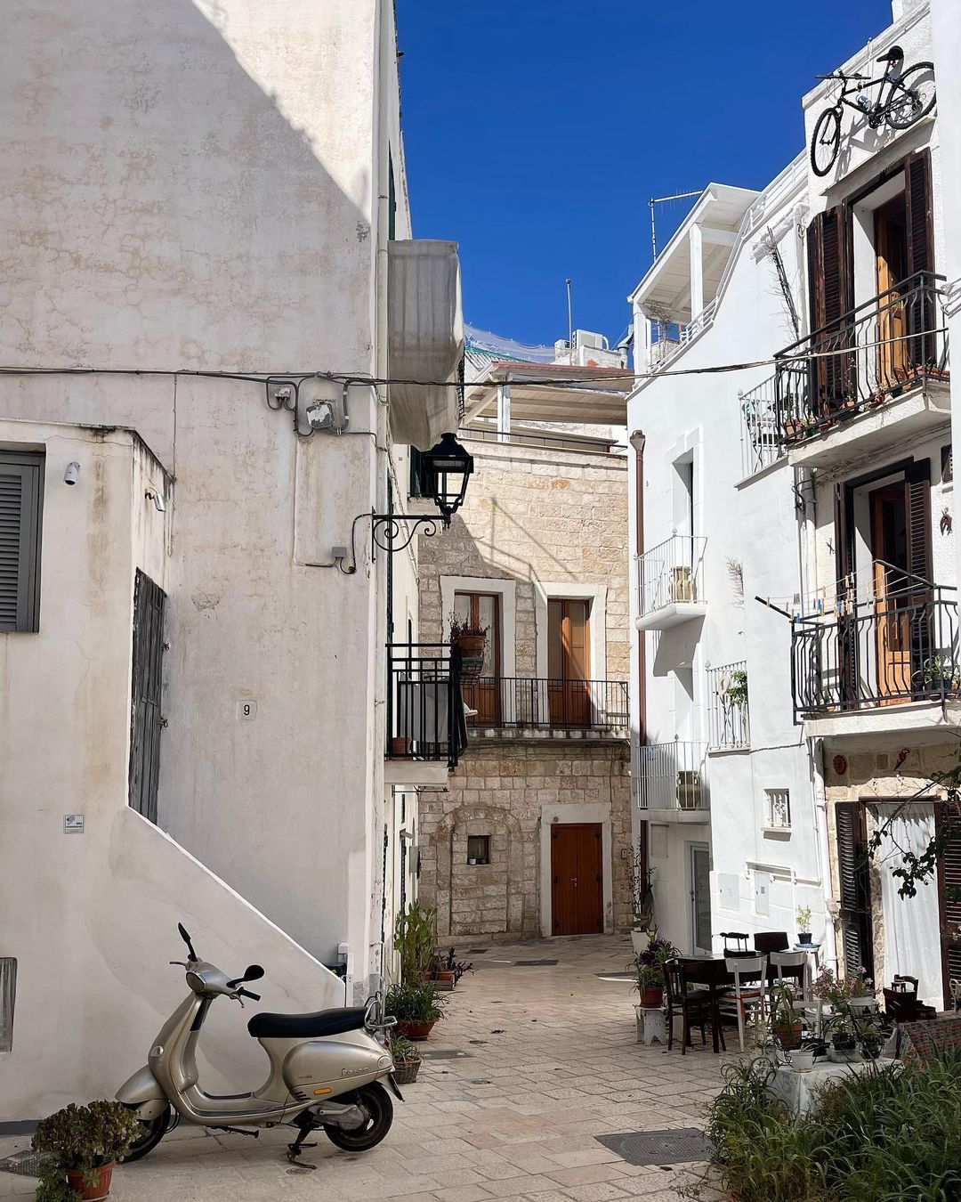 Quaint Italian street scene with a vintage Vespa, traditional white buildings, and clear blue sky, capturing the essence of a peaceful European town.