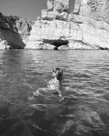 Woman swimming in ocean with large rocky cliffs in background, captured in black and white by Jasmine Hand in Sydney.