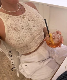 Woman in cream knit sleeveless top holding a stemmed glass with an orange cocktail and ice