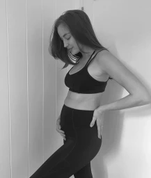Pregnant woman wearing a black sports bra and leggings posing in profile against vertical wood paneling