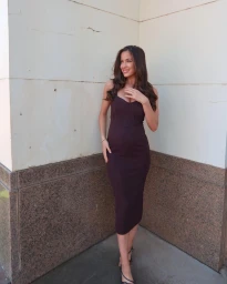 Woman in a dark purple midi dress standing against a pale architectural wall outdoors in Sydney.