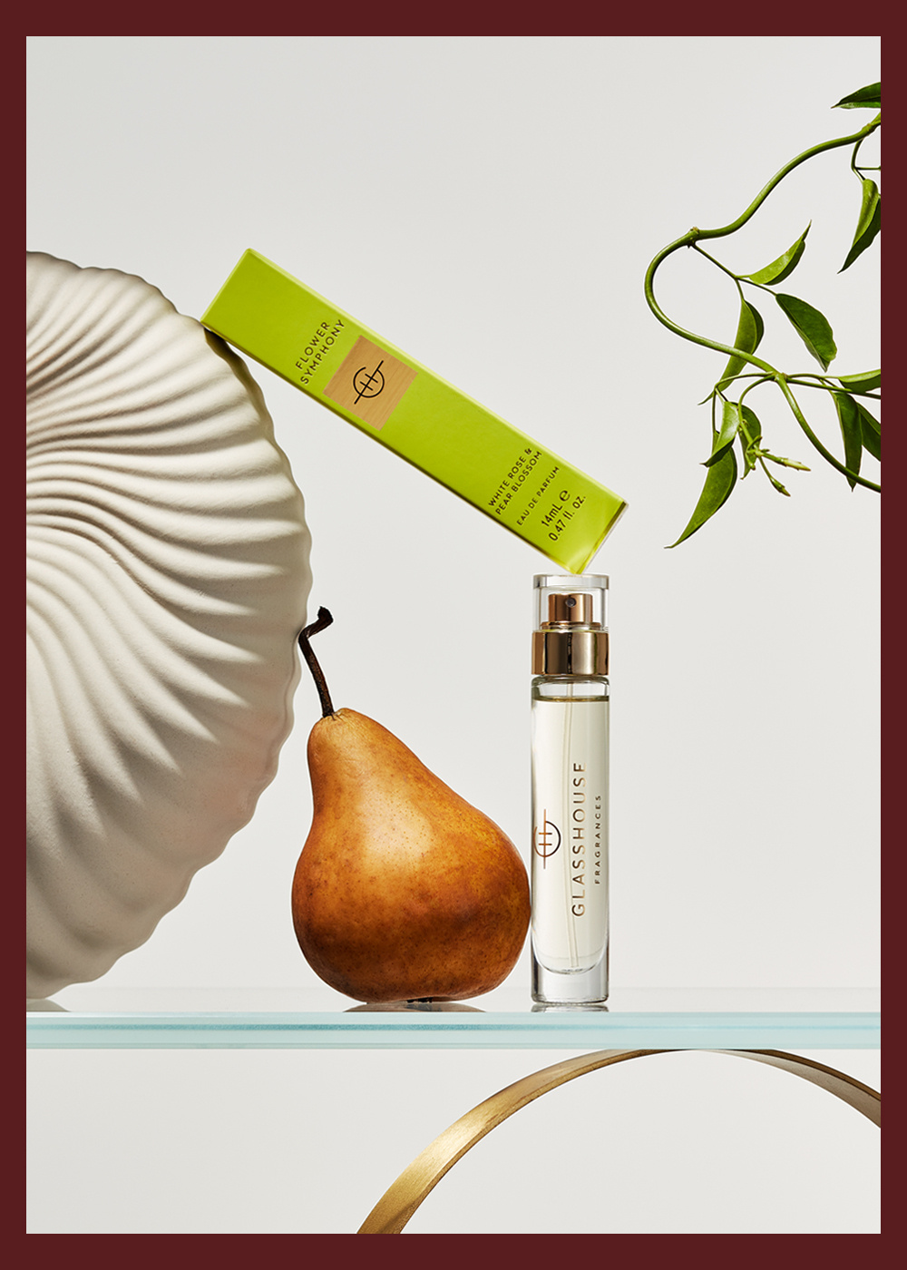 Still life featuring Flowerhouse Fragrances perfume, pear, and skincare on a light blue surface against a white backdrop with plant accents.