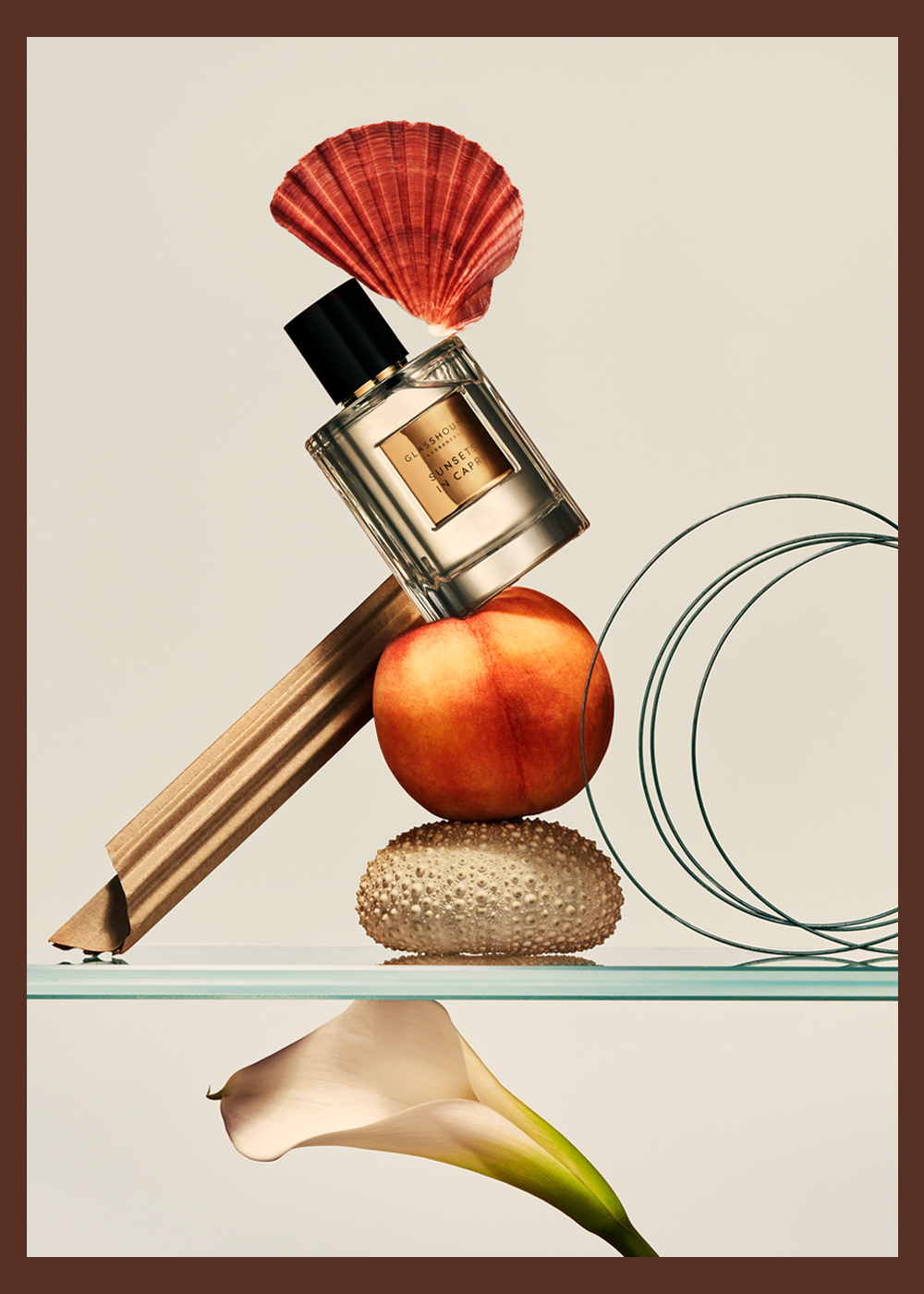 Still life composition featuring a perfume bottle, seashell, peach, sea urchin shell, and calla lily against a neutral backdrop.