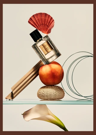Still life composition featuring a perfume bottle, seashell, peach, sea urchin shell, and calla lily against a neutral backdrop.
