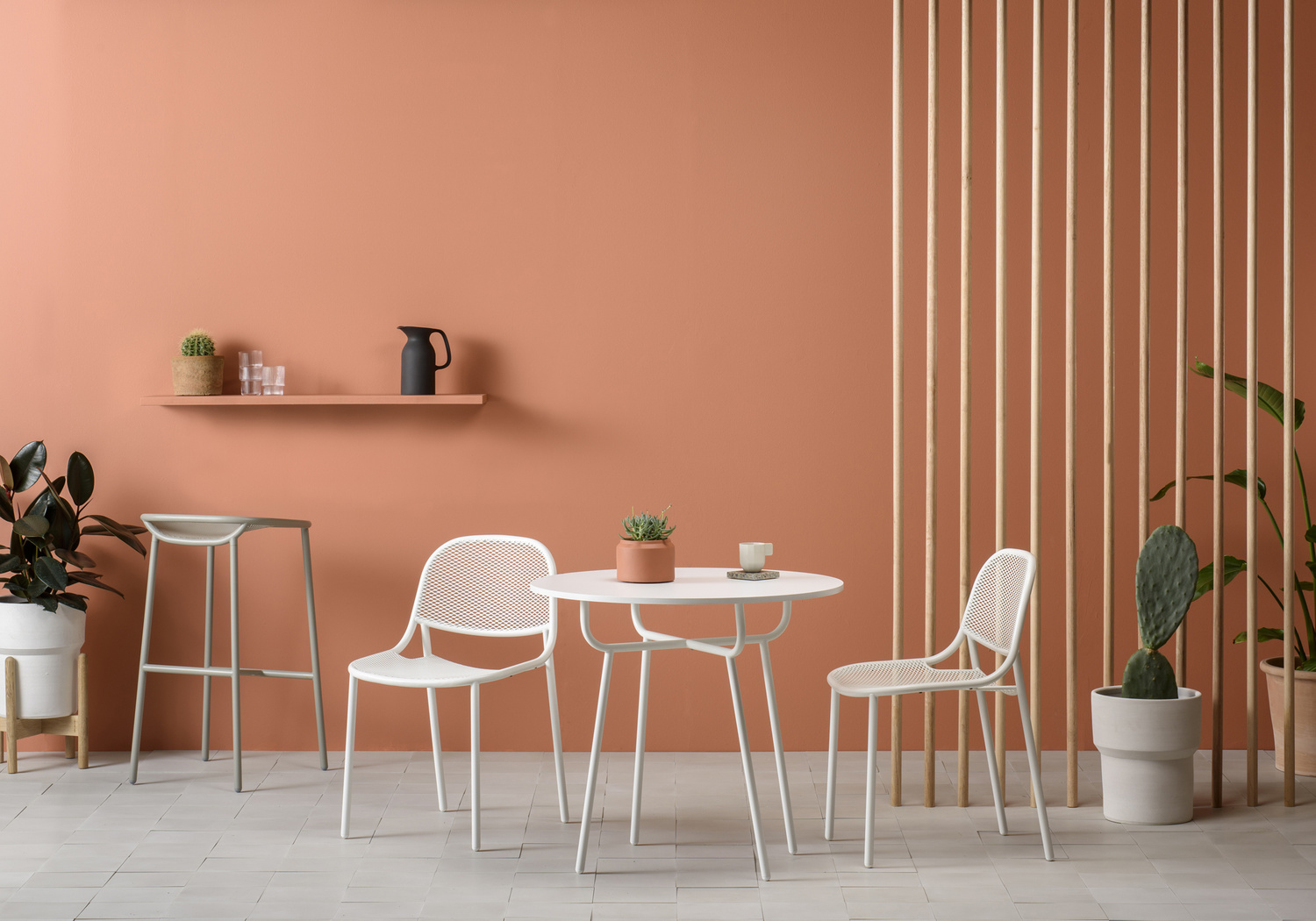 Interior featuring a white round table with chairs, a bar stool, and potted plants against a peach wall and tile flooring.