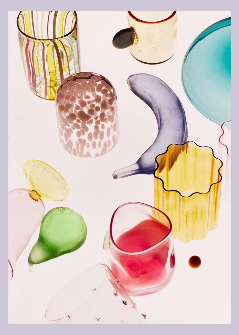 Colorful glass art pieces arranged on a white background. Clear glassware includes cups, decorative objects, and translucent designs.