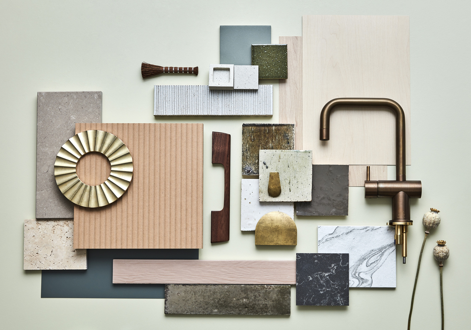 Still life showcasing interior design material samples arranged on a light green surface with a brass faucet and decorative elements.