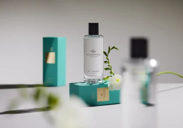 Glasshouse Fragrances room spray bottle standing on a turquoise box with white flowers against a grey background.