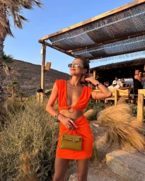 Woman in a vibrant orange cut-out dress wearing sunglasses and holding a small yellow handbag outdoors in Sydney