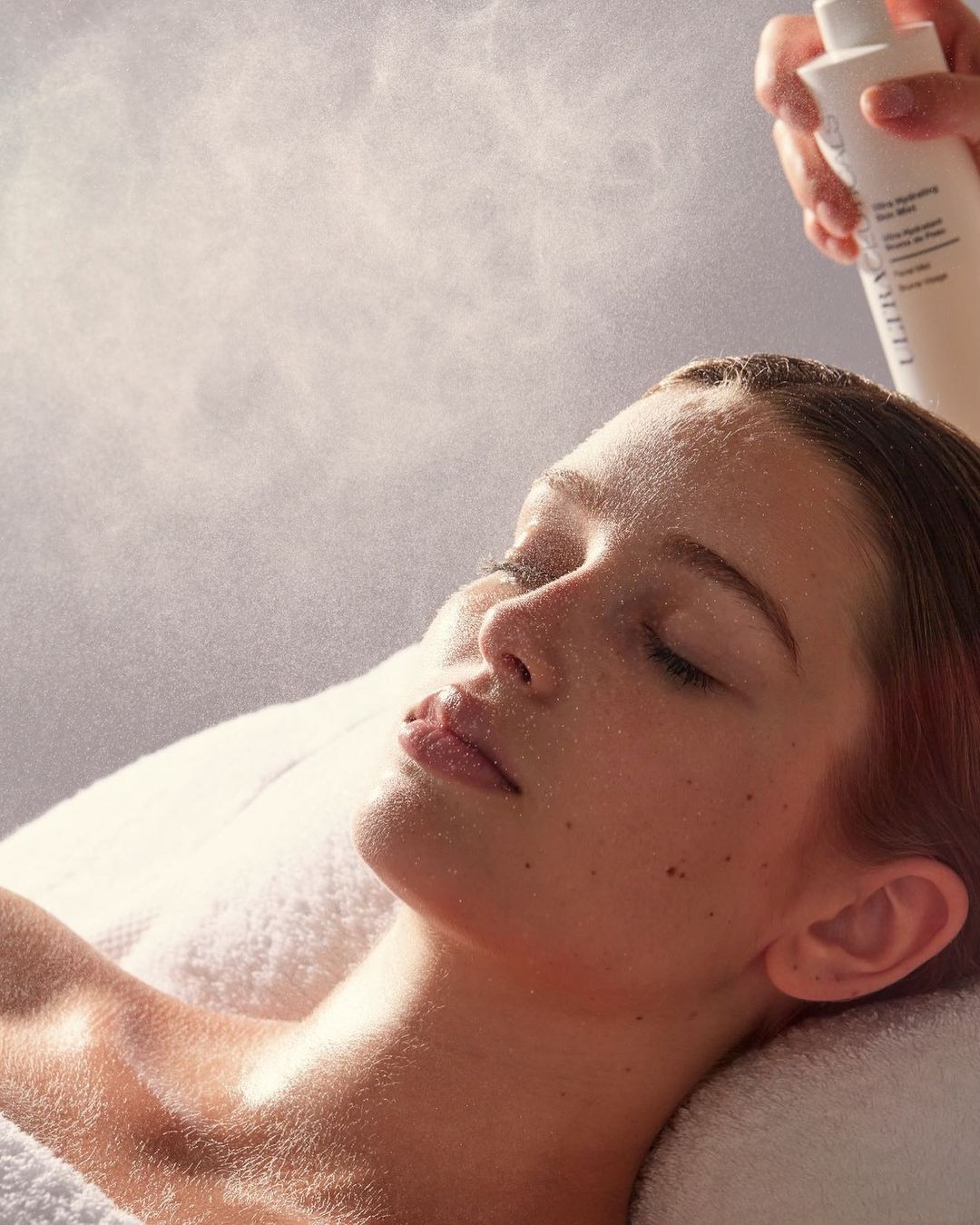 Close-up of a woman's face receiving a hydrating mist. Serene beauty shot with a focus on skincare and the application of the product.