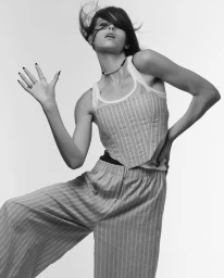 Black and white portrait of a woman in a striped top and wide trousers posing against a plain background