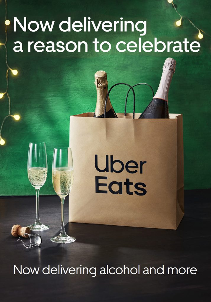 Uber Eats advertisement featuring champagne bottles in a delivery bag, champagne flutes, and the slogan 'Now delivering alcohol and more'.