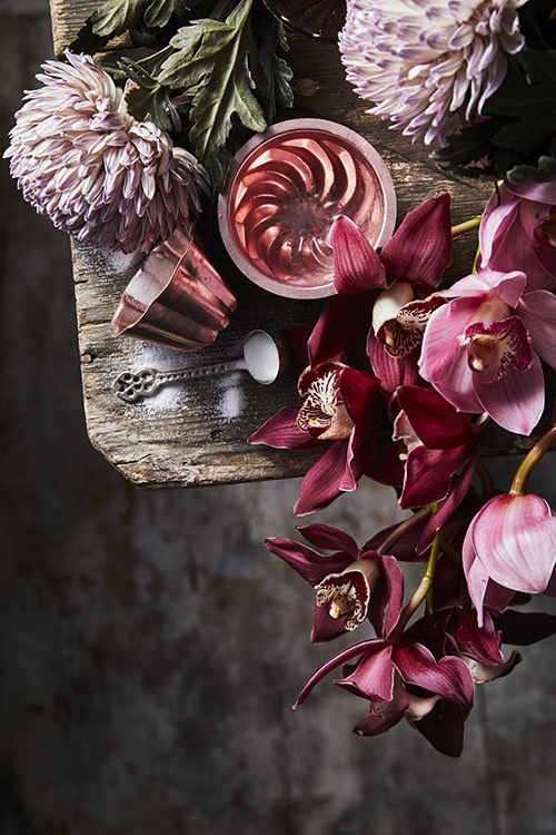 Close-up still life shot featuring flowers, mold, spoon, and white powder arranged on a weathered wooden surface, creating an elegant aesthetic.