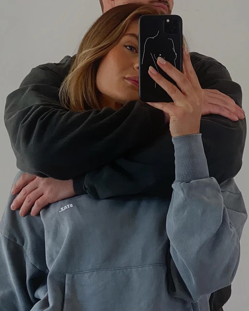 Woman takes selfie with phone case featuring line art of a female figure while a man embraces her from behind.