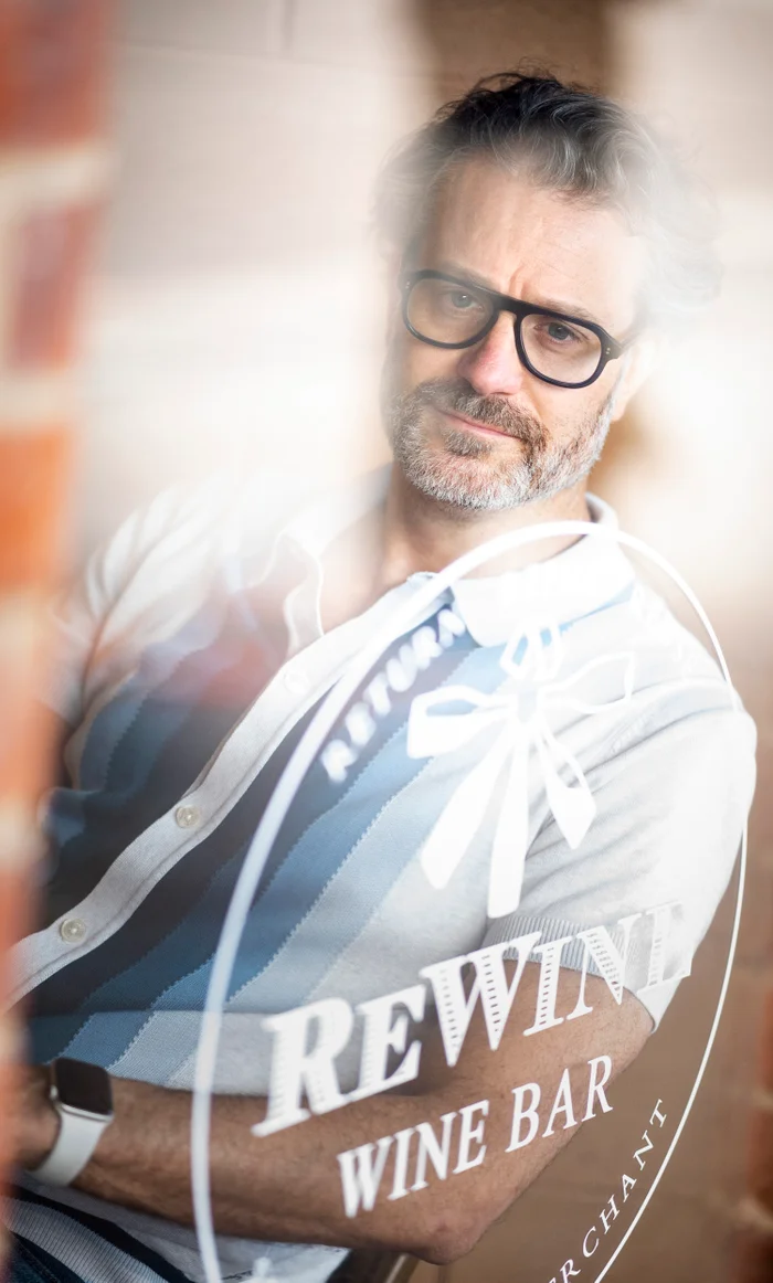 Middle-aged man wearing glasses and a striped polo shirt seated behind a glass window with etched lettering