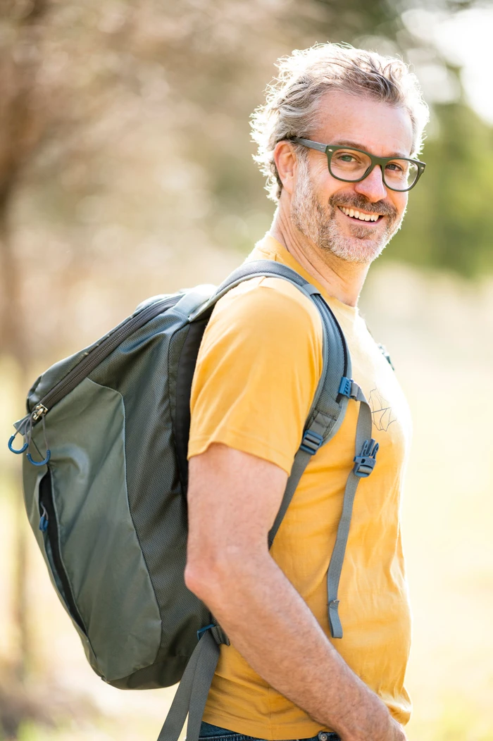 Middle-aged man wearing glasses and a yellow t-shirt carrying a large green backpack outdoors in Sydney.