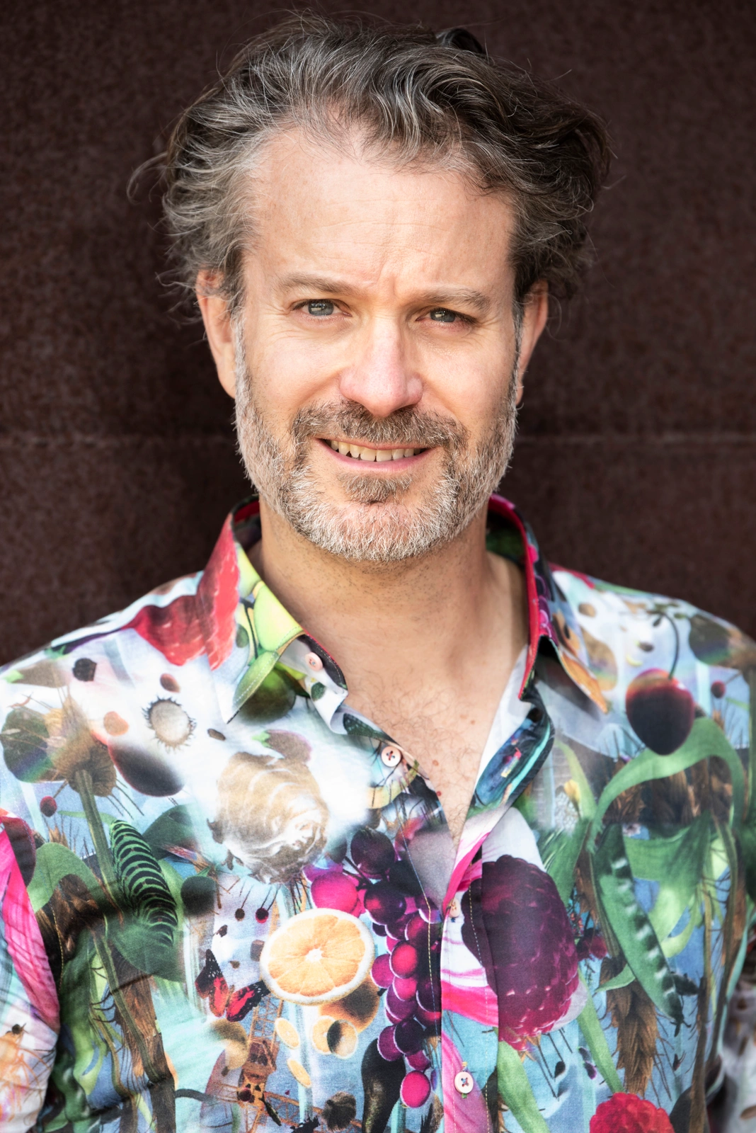 Portrait of a man in his 40s with a beard wearing a vibrant fruit and floral print button-up shirt.