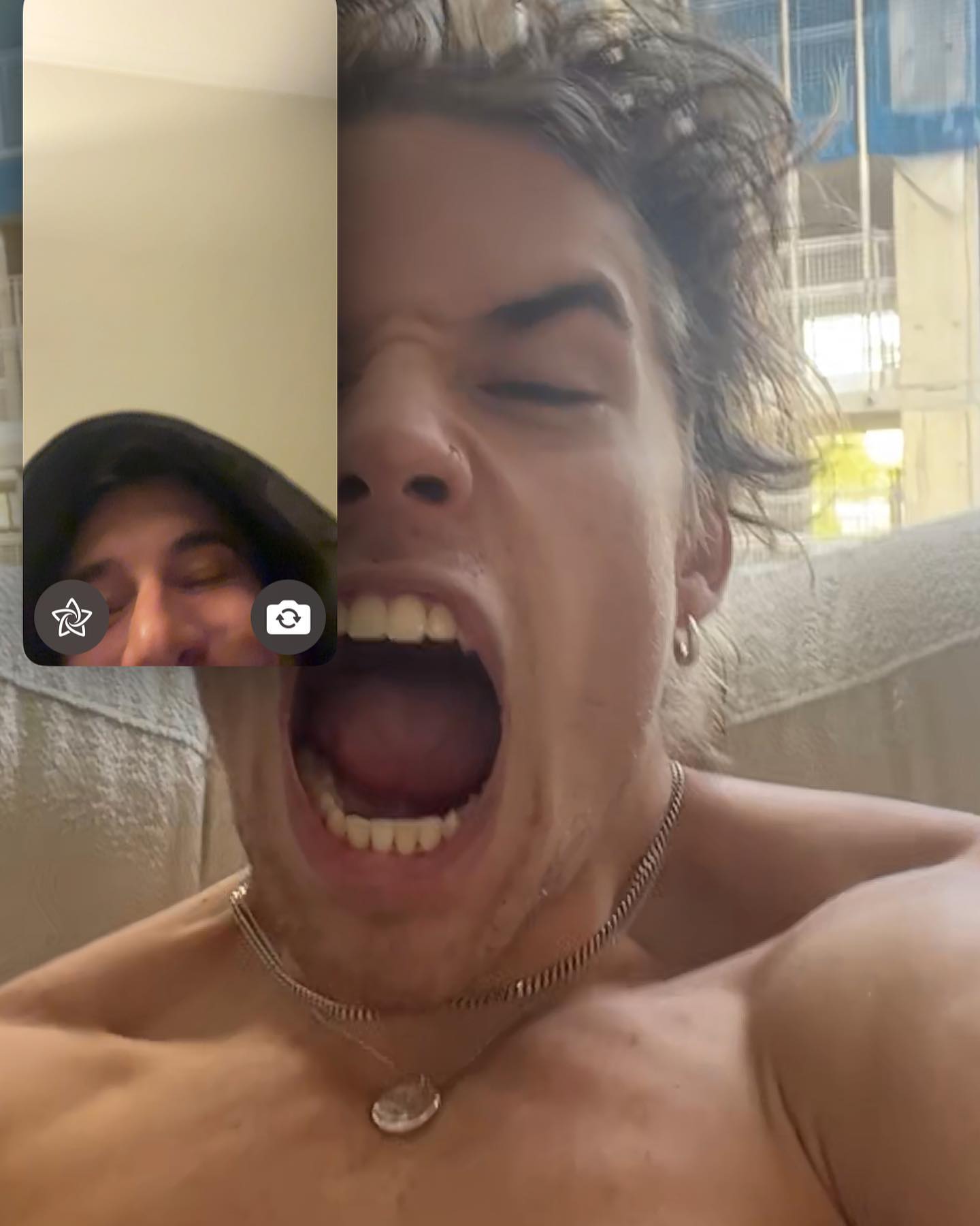 Two young adults in a split screen, one yelling with an open mouth, wearing a silver necklace and earring; the other is looking down.