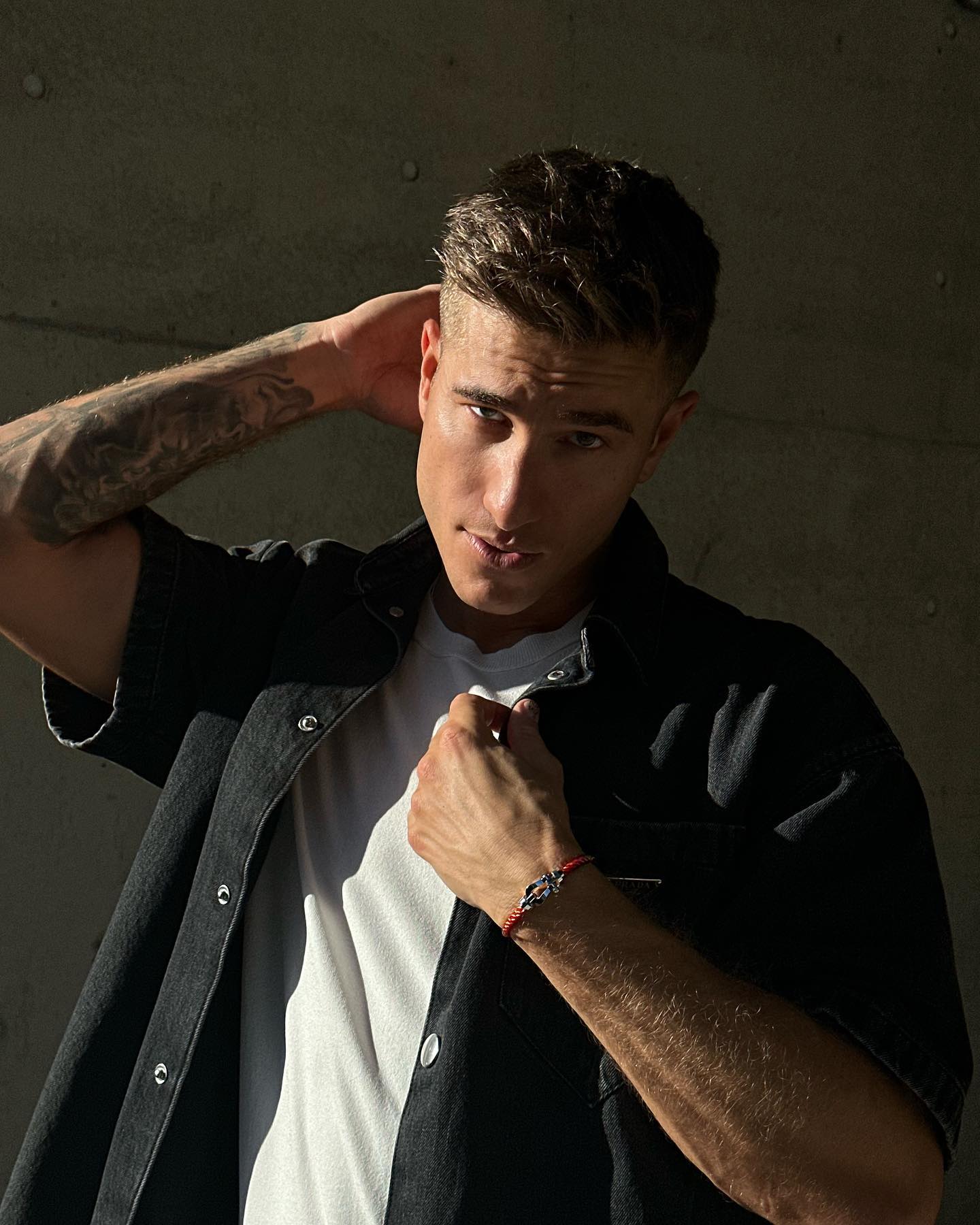Portrait of a light-skinned adult male with short brown hair wearing a short-sleeve button-down shirt and red bracelet, posing indoors.