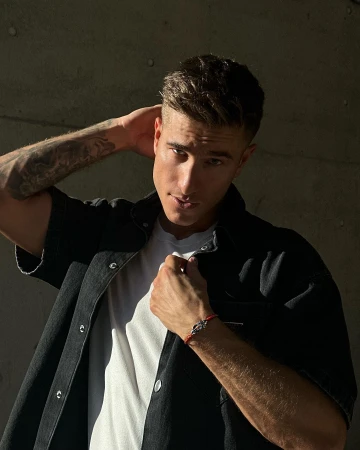 Portrait of a light-skinned adult male with short brown hair wearing a short-sleeve button-down shirt and red bracelet, posing indoors.