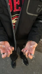 Close-up overhead shot of hands displaying custom nail art and rings, wearing a black jacket and graphic hoodie.