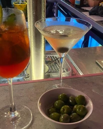 Two cocktails in stemmed glassware and a small bowl of green olives on a bar counter in Sydney by Kate Robinson