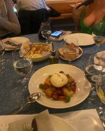 Burrata salad and wine glasses on a blue restaurant table with people dining