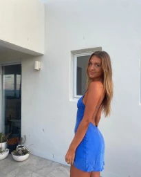 Young woman in a backless blue mini dress posing against a white exterior wall in Sydney by Kate Robinson.