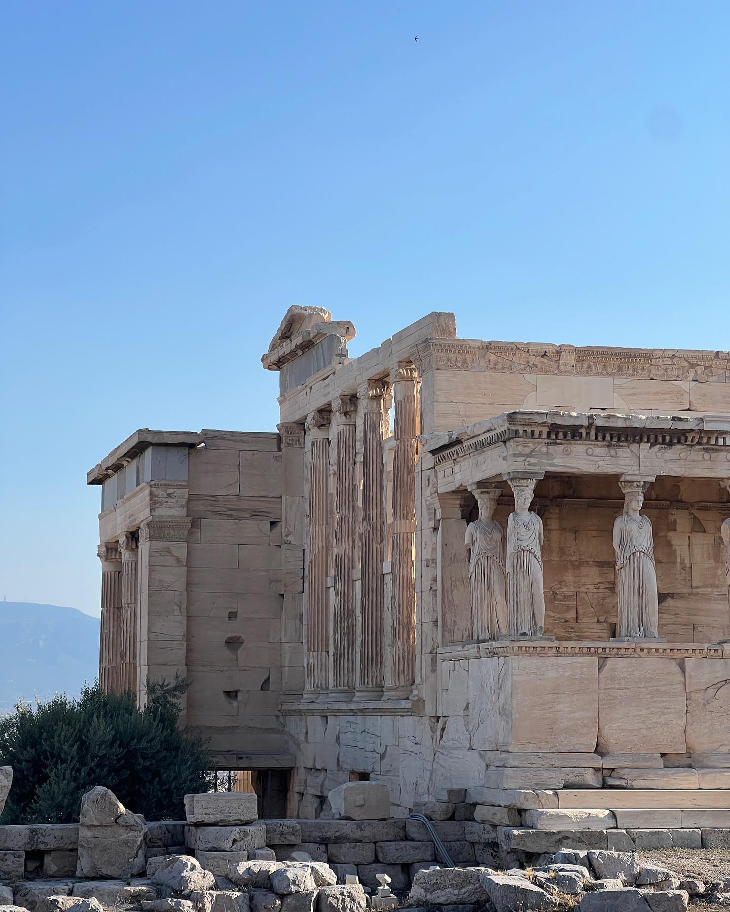 Ancient Greek architecture of the Erechtheion temple, featuring classical columns, statues, and stonework, set against a clear blue sky.
