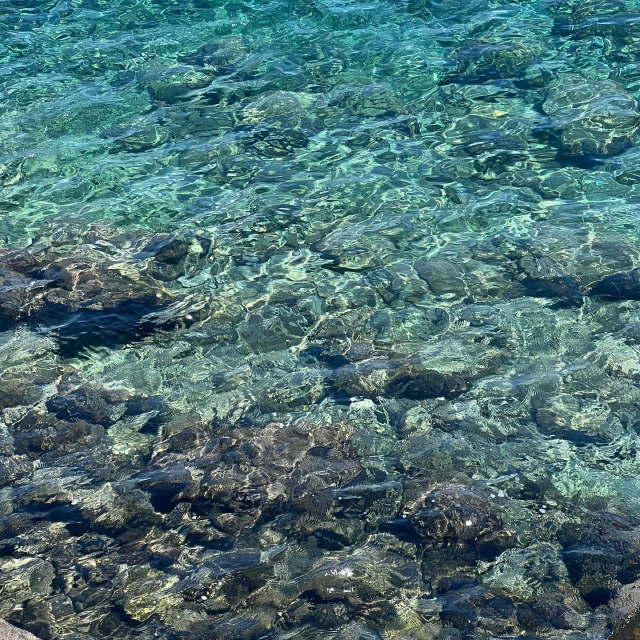 Close-up of crystal-clear turquoise sea water rippling over rocky seabed, creating a textured, natural underwater view.