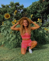 Woman in red gingham athletic wear and straw hat crouching in front of tall sunflowers in Sydney by Kerry Knight