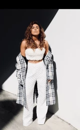 Woman in white strapless crop top and white trousers with a plaid coat draped over her shoulders outdoors.