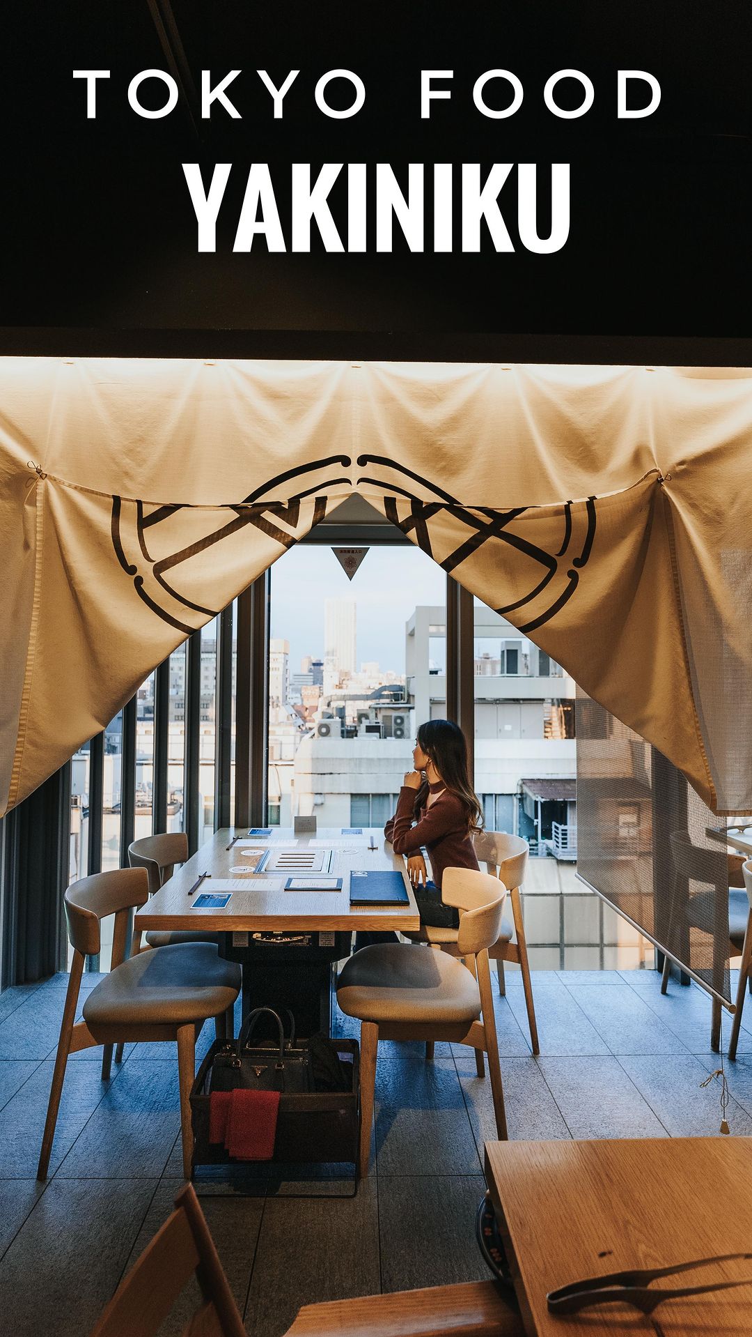 Woman seated at a restaurant table looking out a window towards a city view under a fabric doorway curtain
