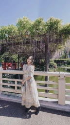Woman wearing a patterned dress standing on a bridge beneath a wisteria pergola in a park captured by Kim Dao.