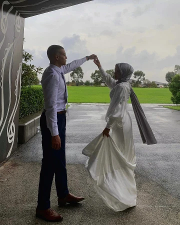 A man in a white shirt and blue trousers dancing with a woman in a white dress and grey hijab outdoors in Sydney.