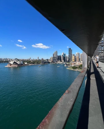Sydney Harbour with the Opera House and city skyline in the background, seen from the Sydney Harbour Bridge, with a person walking.