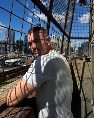 Man stands on a building looking at city skyline behind a steel cage. The bright daylight shot emphasizes the urban environment.