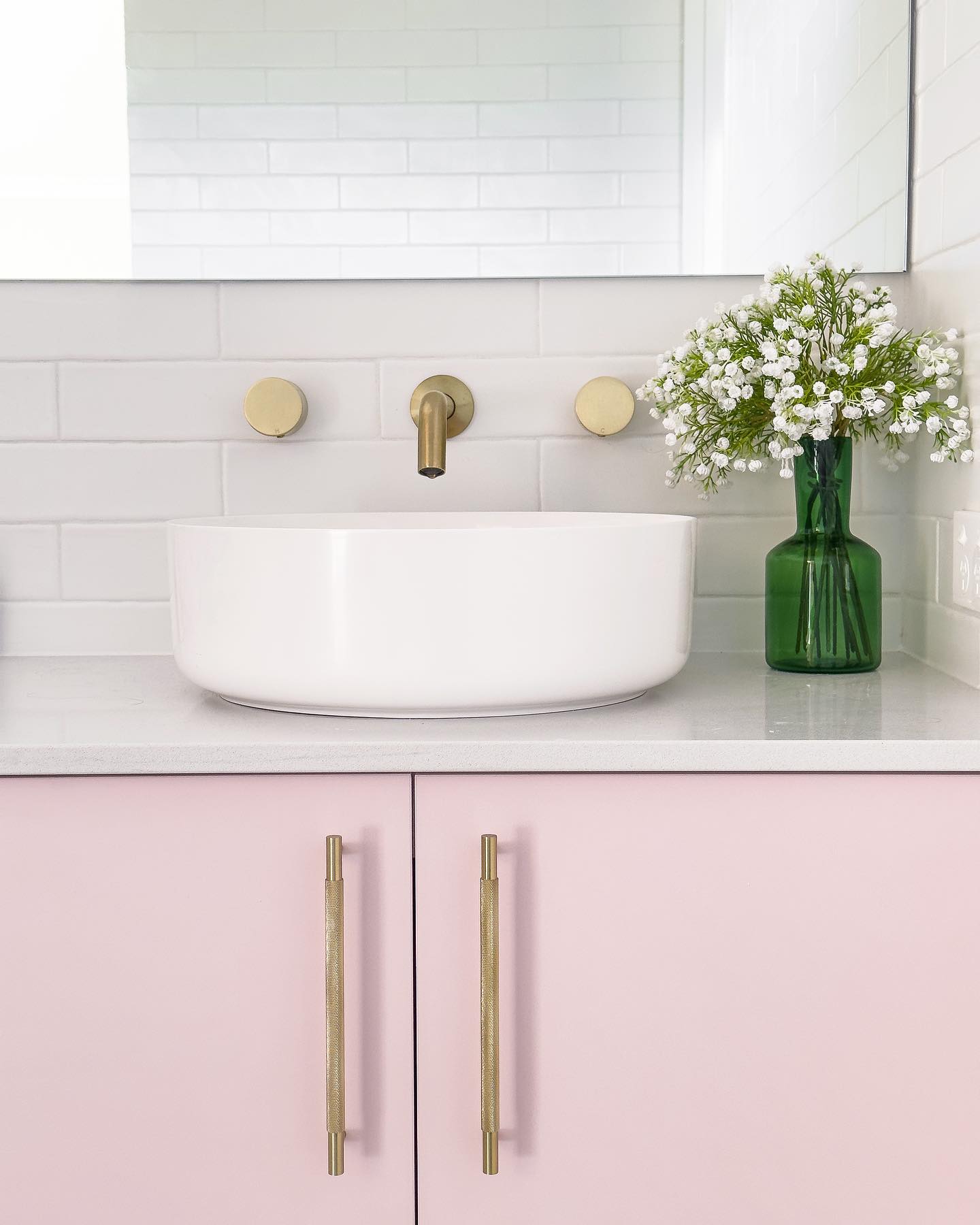 Bathroom interior featuring white countertop sink with brass faucet and cabinet hardware, white subway tile, and small white flowers.