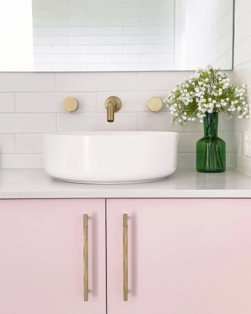 Bathroom interior featuring white countertop sink with brass faucet and cabinet hardware, white subway tile, and small white flowers.