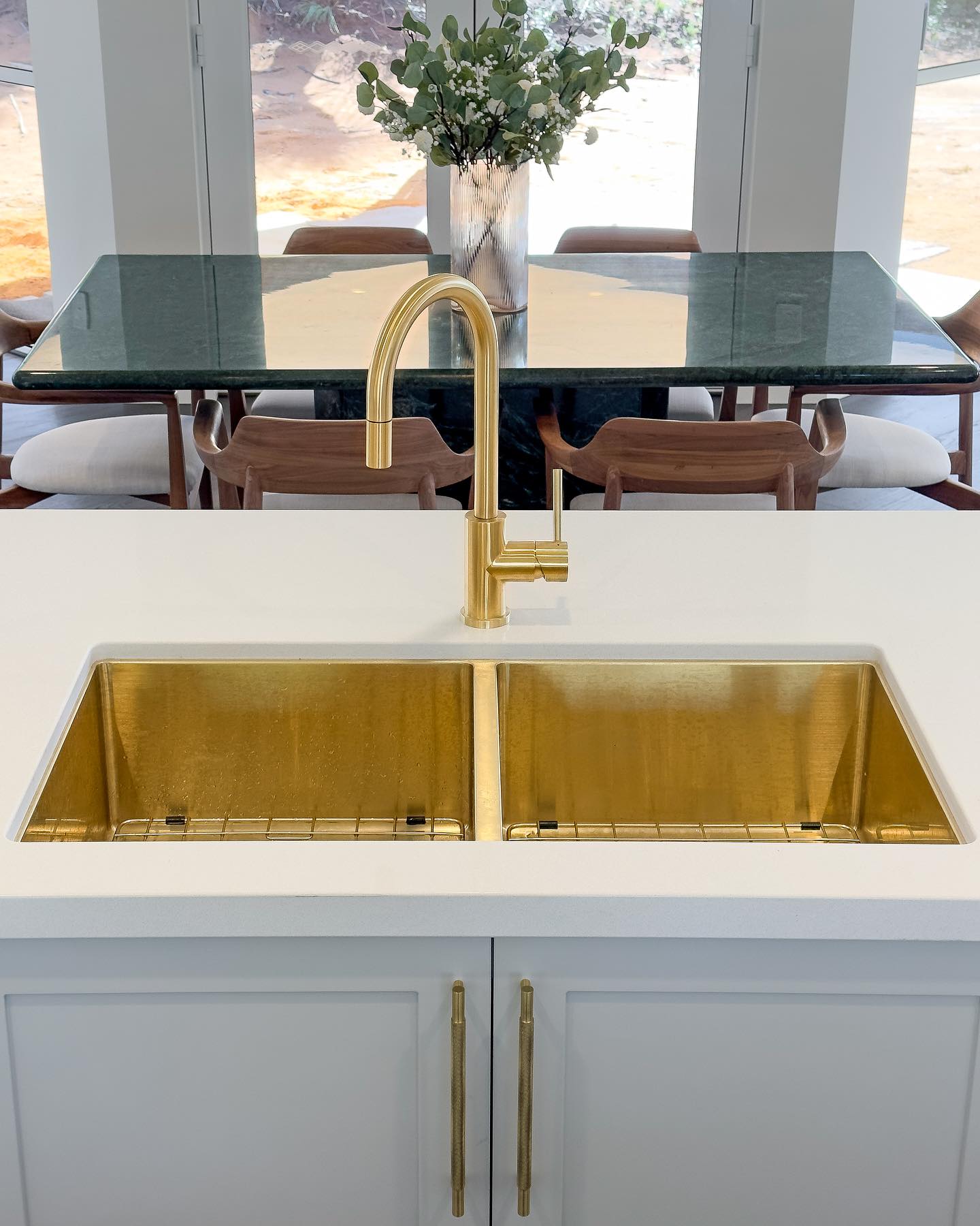 An interior shot showcases a modern kitchen sink with a gold faucet, set against a backdrop of a marble table and natural light.
