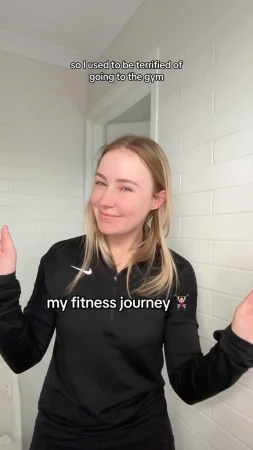 Content creator Lauren Curtis in a black athletic zip top standing against white tiled walls