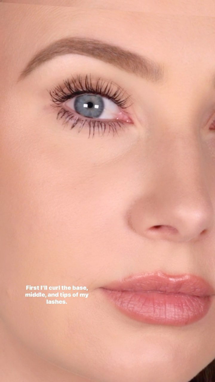Close-up of a woman's face focuses on her eye with mascara-coated lashes, eyebrow, and lips with a pale pink tint. Beauty shot.