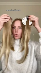 Woman holding up hair extensions in front of her face wearing a white zip sweatshirt