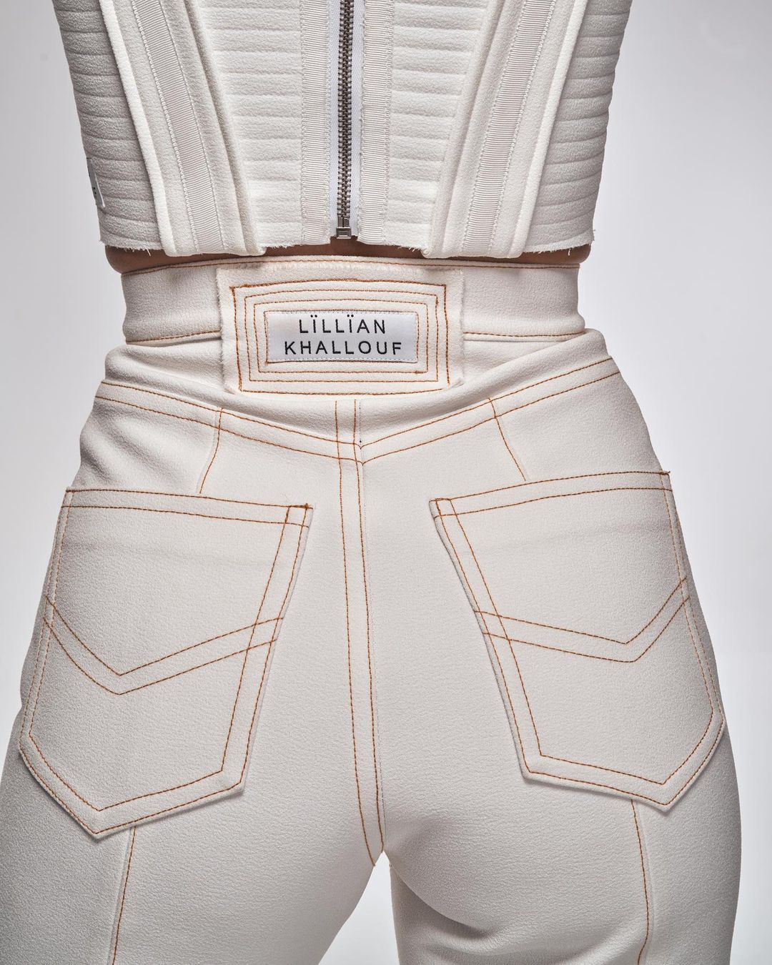 Close-up shot of white high-waisted pants with orange stitching and a matching top, showcasing fashion details and neutral tones.
